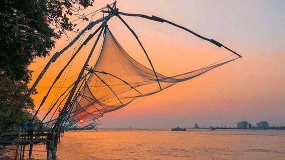 A traditional Chinese fishing net silhouetted against a colorful sky at dusk or dawn over a body of water.