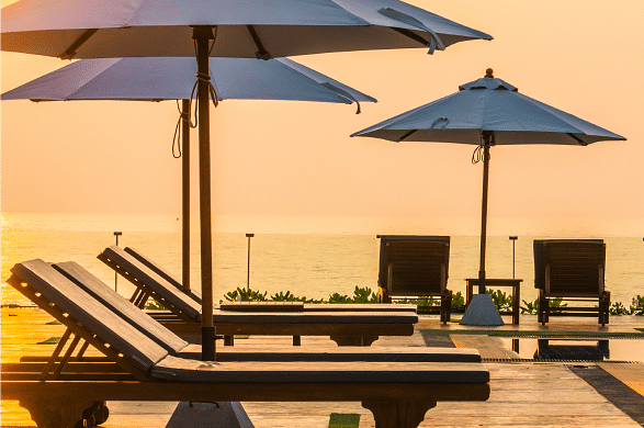 A luxurious poolside setting with sun loungers and umbrellas, overlooking a stunning sunset view.