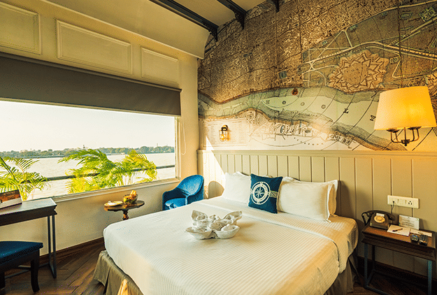 Room at Polo Floatel Kolkata with a bed, decorative map mural, and window-side seating with river view.