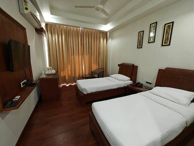A spacious Luxury Room with two single beds along with beige coloured curtains covering the windows - Hotel Gold, Panipat