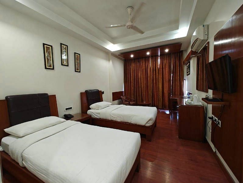 A bedroom with two single beds and dark wooden flooring along with a wall mounted television - Hotel Gold, Panipat