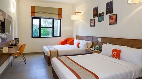 View of two beds arranged in a hotel room with a large window and natural lighting- Max Hotel Prayagraj.