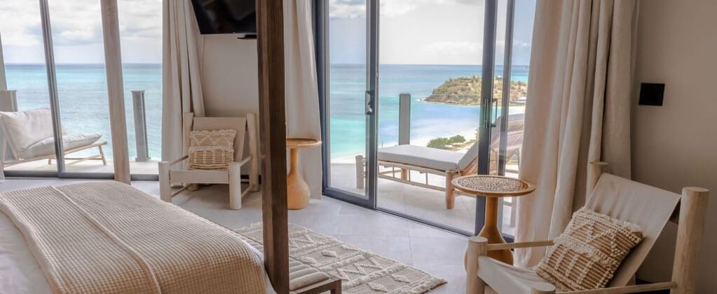 A sea-facing room with wooden furniture, large glass doors, and a balcony overlooking the ocean.