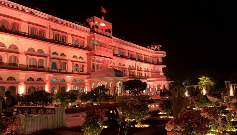 Front Facade of  Umaid Palace Dausa featuring a stretched and multi storey building lit with red light at night for an event.