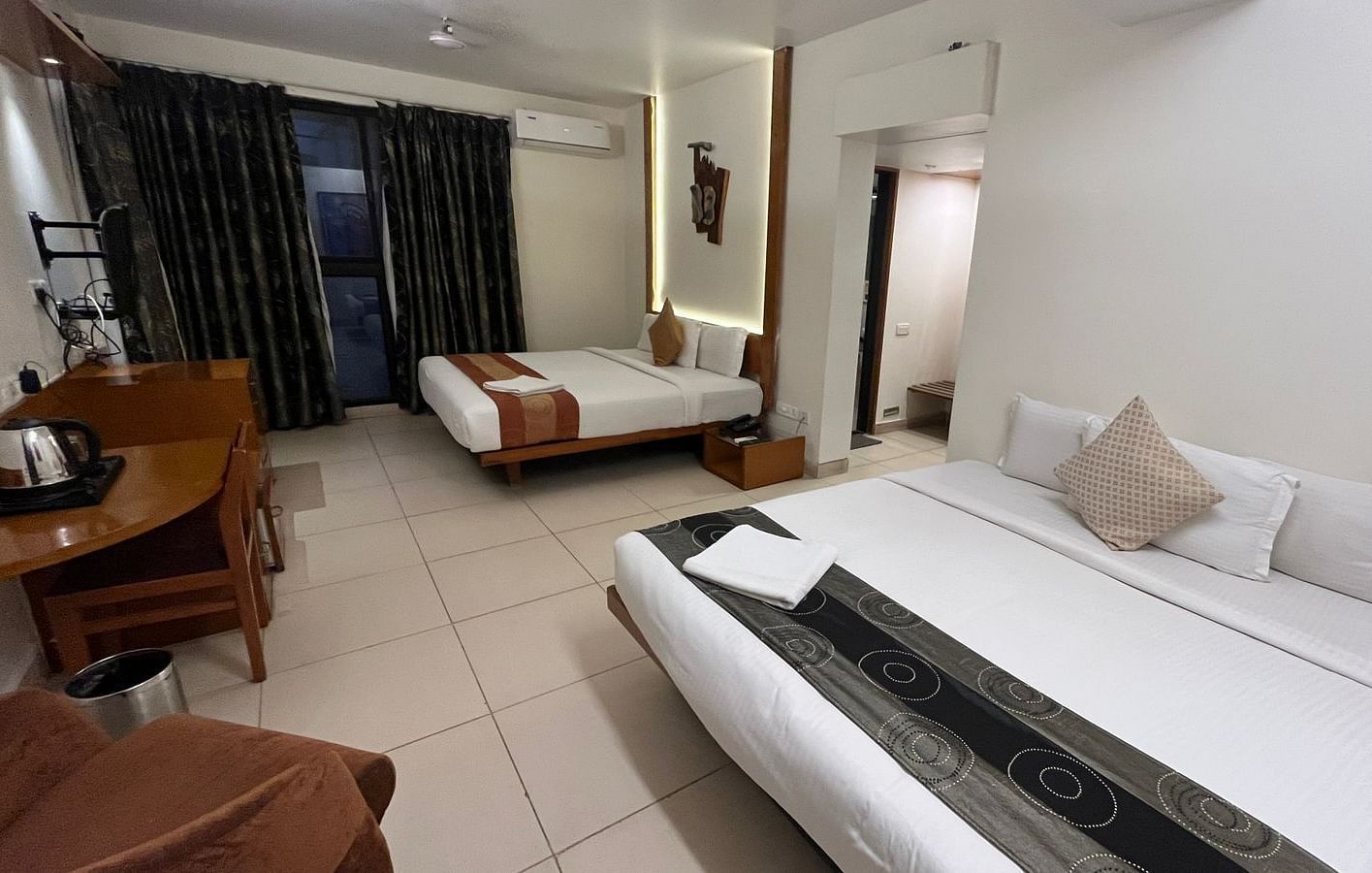 Interior view of a hotel room featuring two beds with white linens and decorative runners, a wooden desk with a kettle, and dark patterned curtains - Astra Hotels & Suites, Spice Garden Layout