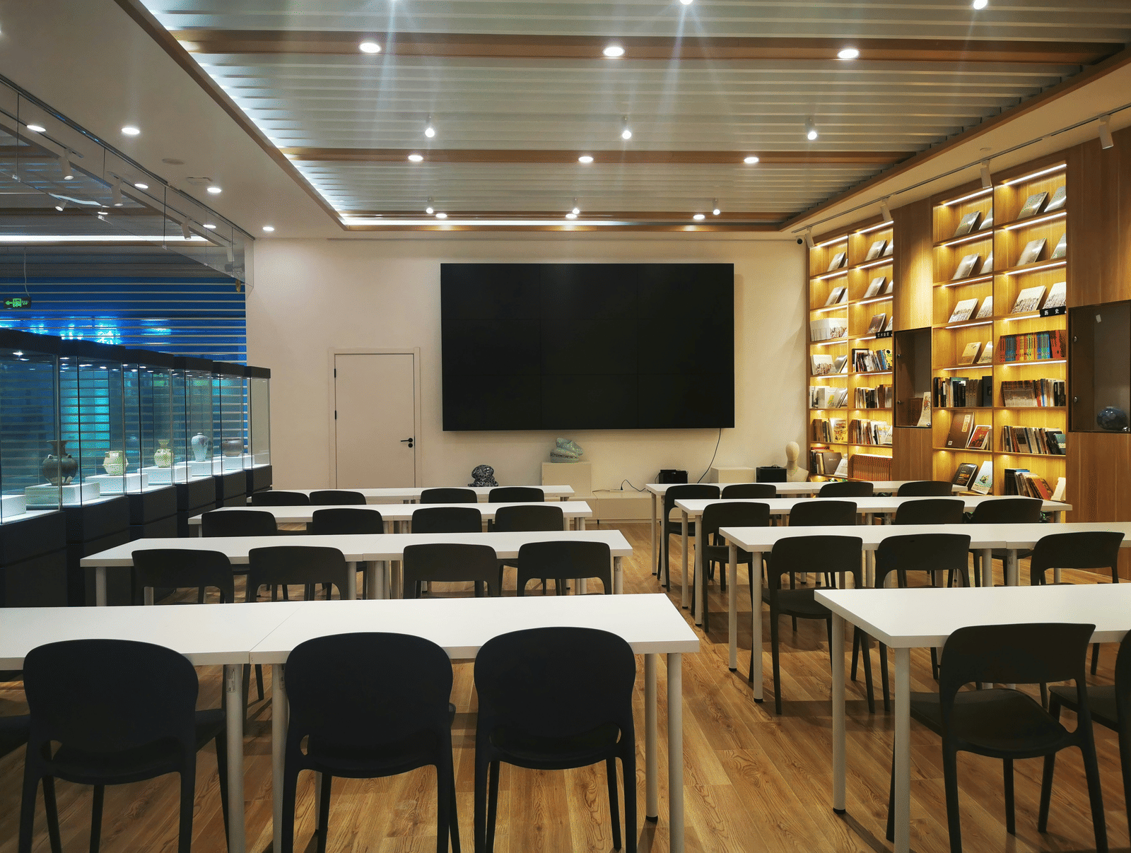A meeting area with tables, chairs, and a television on the wall.