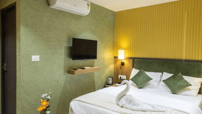 Cosy hotel room featuring a bed, green feature wall, wall-mounted television, and air conditioning unit.