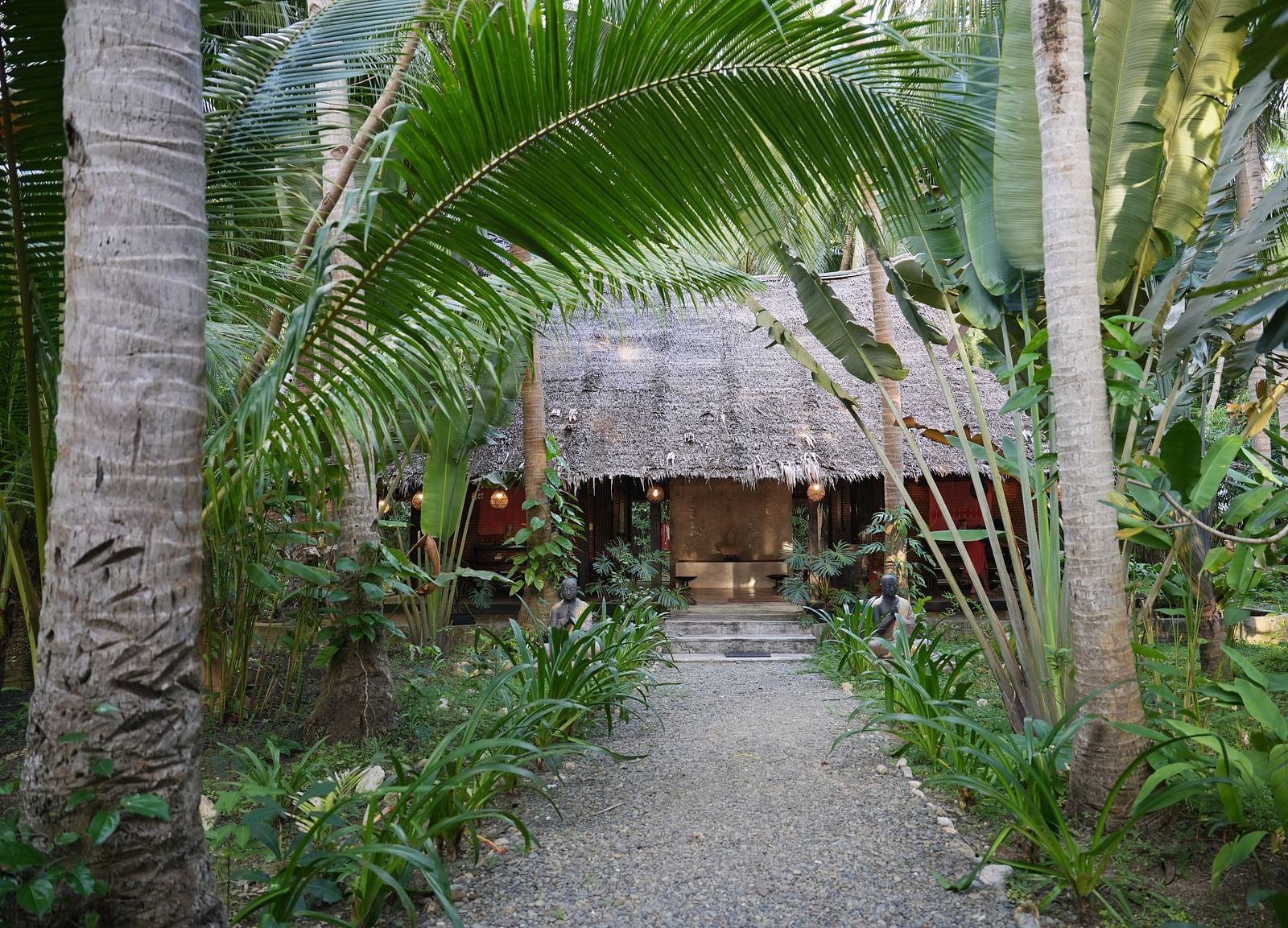 Thatched hut along a narrow pathway surrounded by palm trees at Flower Island Resort.