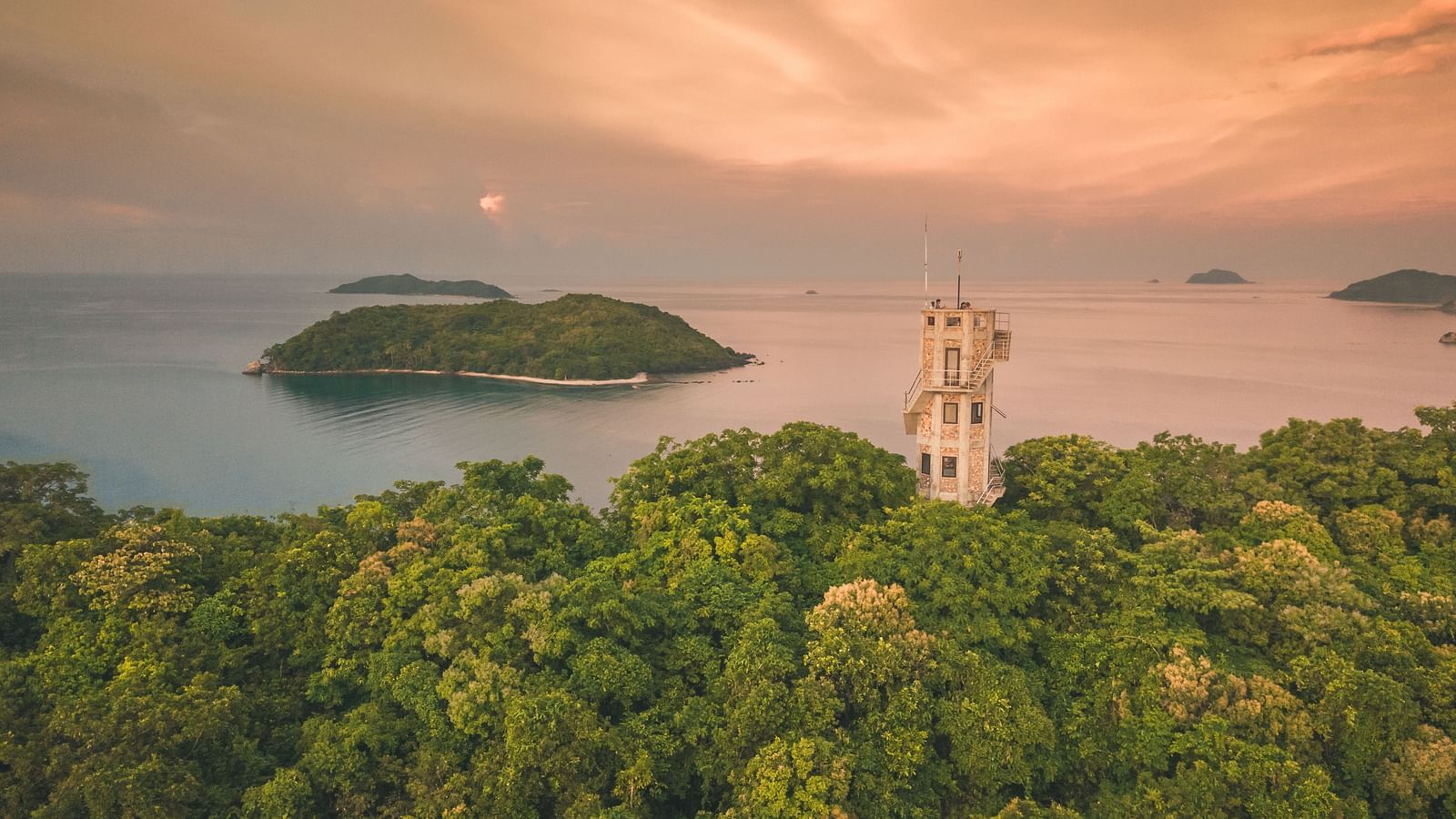 Aerial view of a green island with a white tower structure near Flower Island Resort.