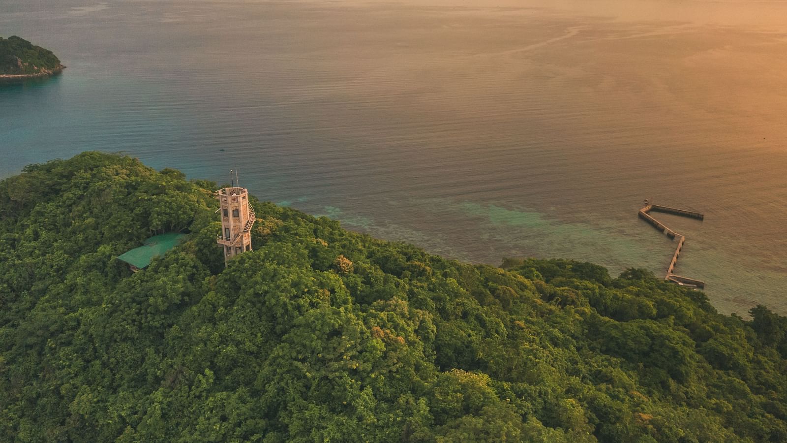 Aerial view of a green hill with a white tower and sea in the background at Flower Island Resort.