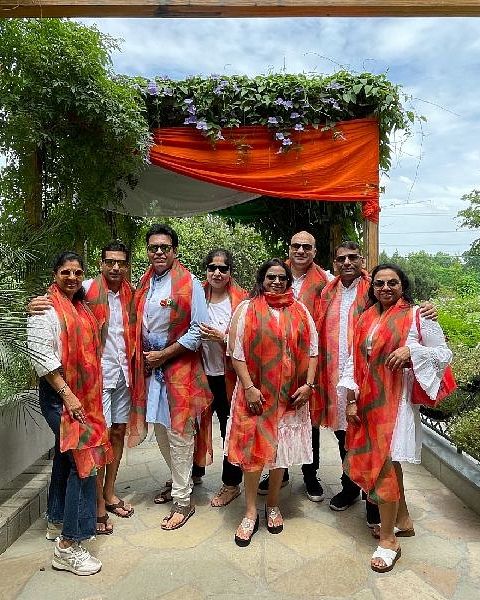 A group of people wearing coordinated saffron shawls and standing in one of the pathways that's bordered on both sides by plants at Karma Chalets.