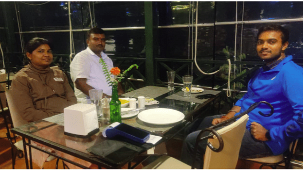 Three guests seated at a glass dining table indoors, enjoying a meal with elegant table settings.