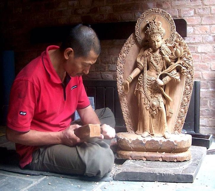 An overview of a man sculpting an idol from wood with accurate hits of the hammer.