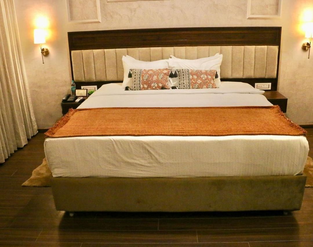 A neatly made bed with white and orange linens of Luxury Junior Suite at Nalapad Hotel Bangalore International.