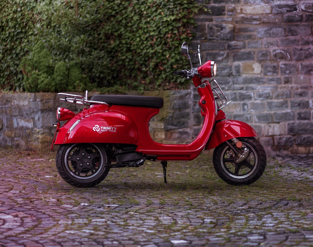 A red scooter parked on a cobblestone ground next to a stone or brick wall