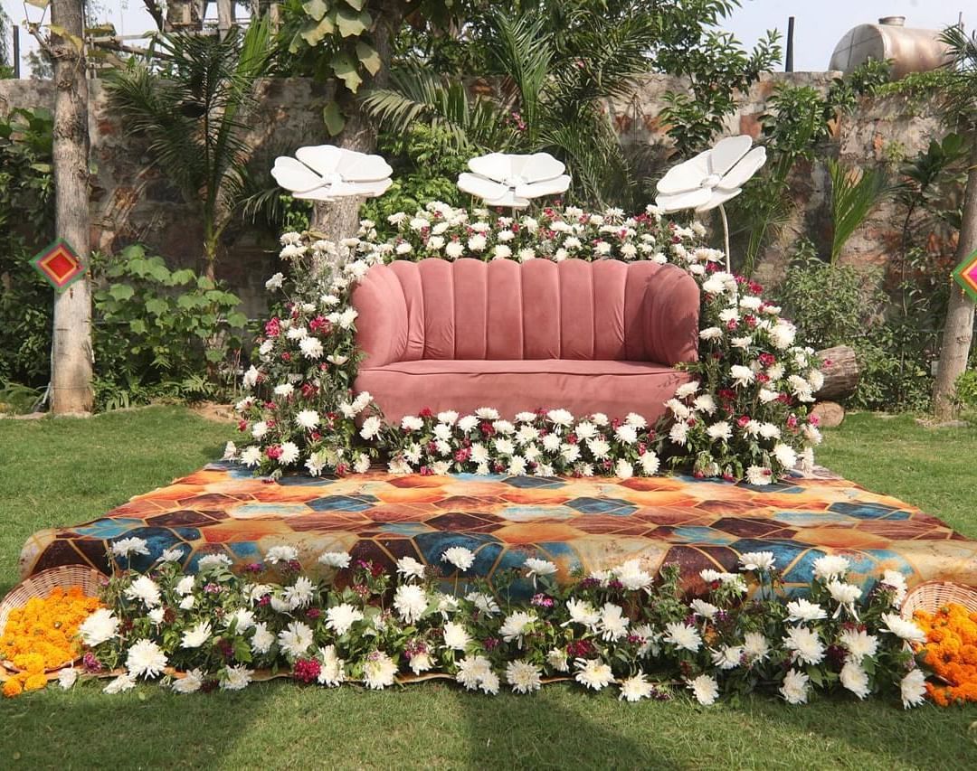 Floral wedding stage at Tisya Farms, Gurgaon with a cushioned seat, flower decorations, and a green lawn.
