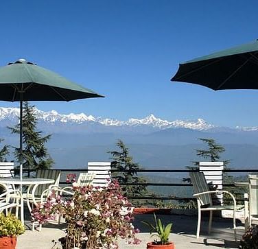 Outdoor dining area with tables and chairs on a balcony, overlooking a breathtaking mountain vista.