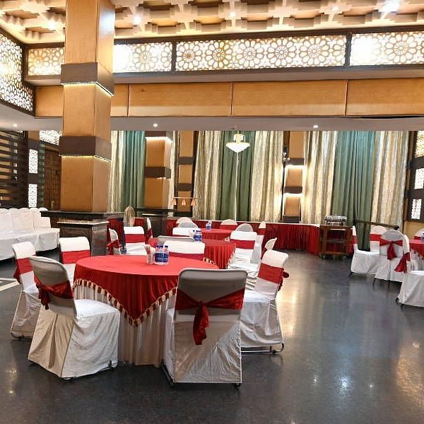 A beautiful conference hall with elegant lights in the ceiling featuring round tables set up all across the hall at Hotel Gold, Panipat.