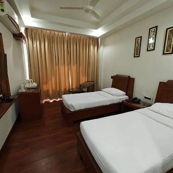A spacious Luxury Room with two single beds along with beige coloured curtains covering the windows - Hotel Gold, Panipat