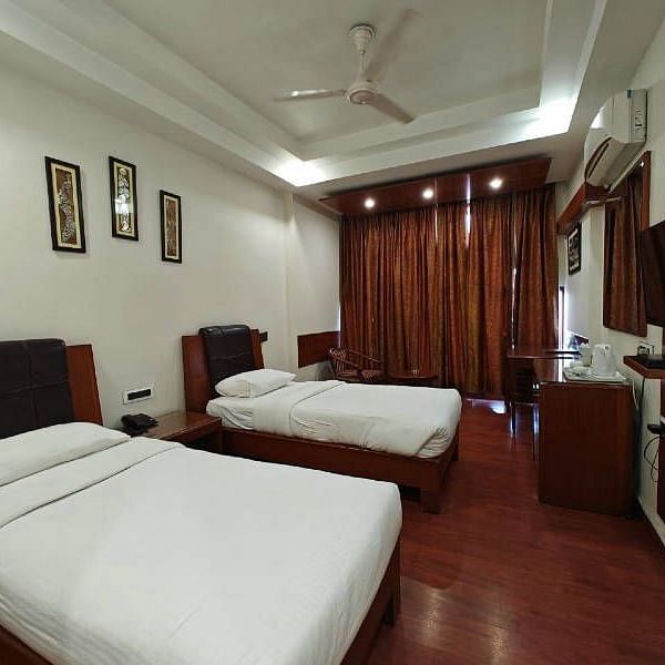 A bedroom with two single beds and dark wooden flooring along with a wall mounted television - Hotel Gold, Panipat