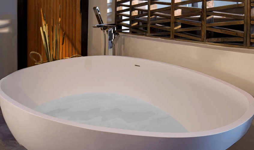 A modern white bathtub filled with water is placed in a well-lit bathroom with a window view.