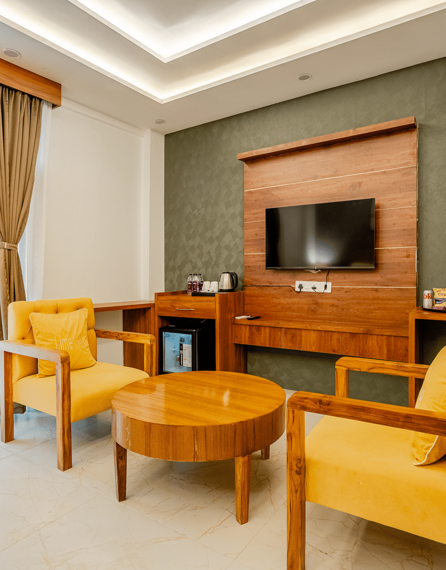 Elegant hotel room seating space with yellow upholstered armchairs, a wooden coffee table, and a wall-mounted TV.