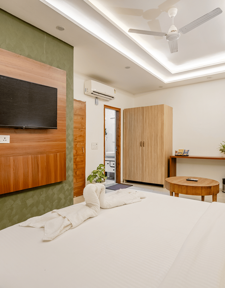 Modern hotel room with a wall-mounted TV on a wooden panel, white bed linen, and a yellow cushion.