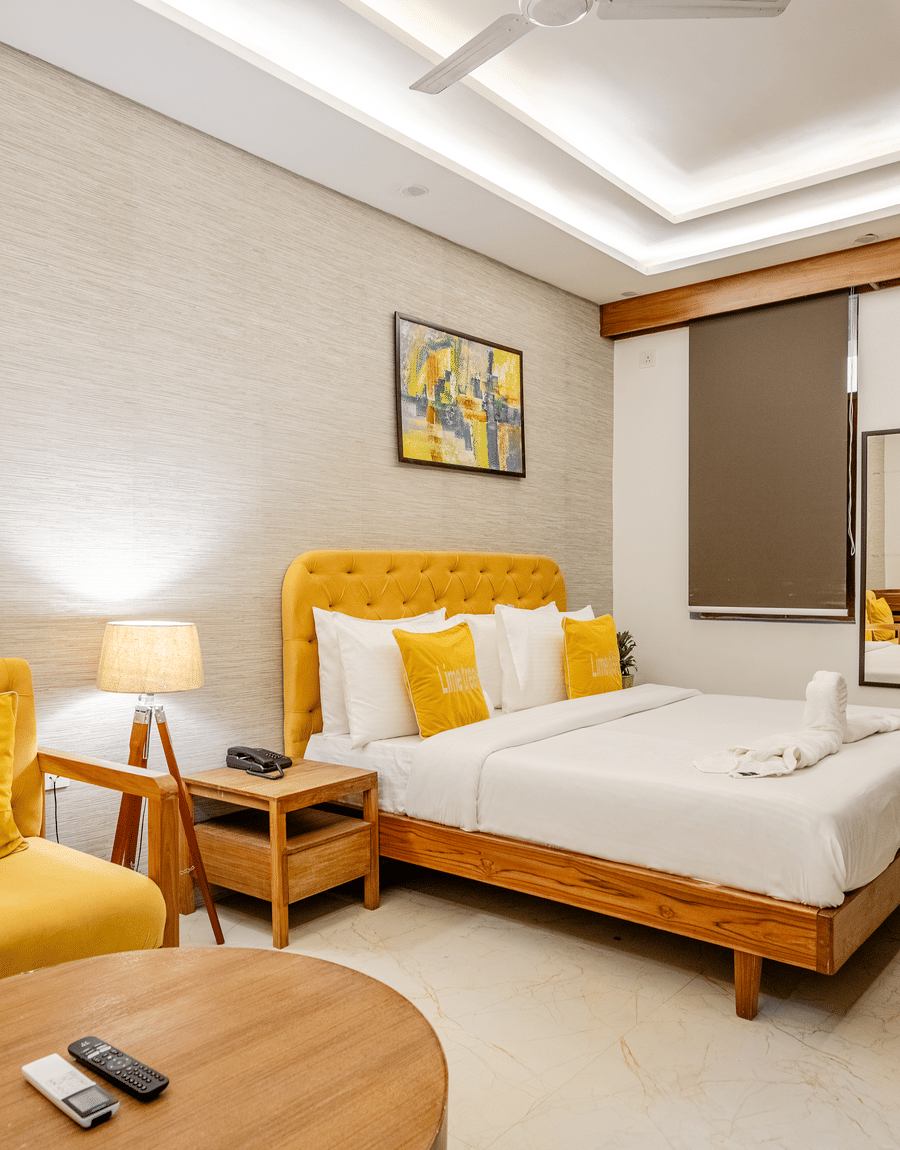 Well-lit hotel guest room displaying a yellow upholstered sofa chair and a double bed.