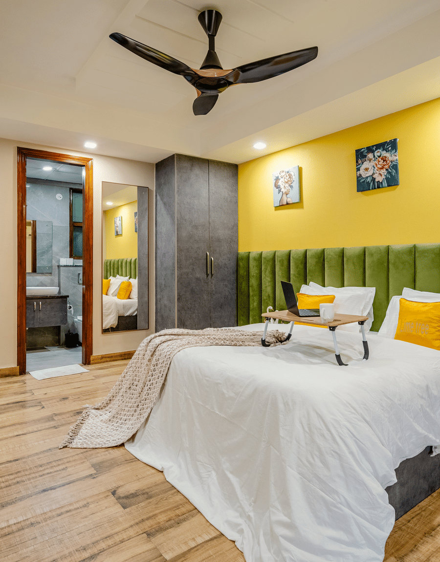 Double bed with a green headboard and laptop tray by a yellow wall in the Superior Double Room, Lime Tree Near Medanta