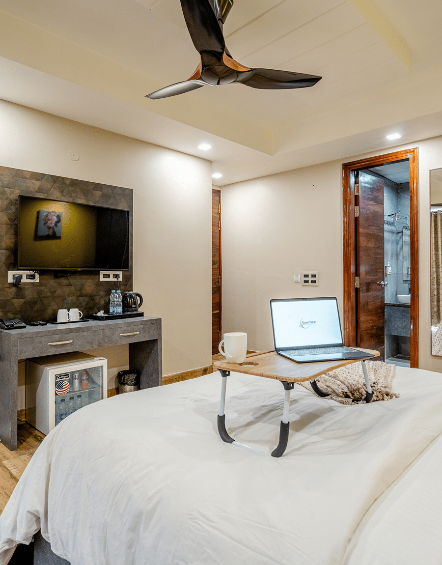 Double bed with a laptop on a tray facing a wall-mounted TV in the Superior Double Room at Lime Tree Hotel Near Medanta
