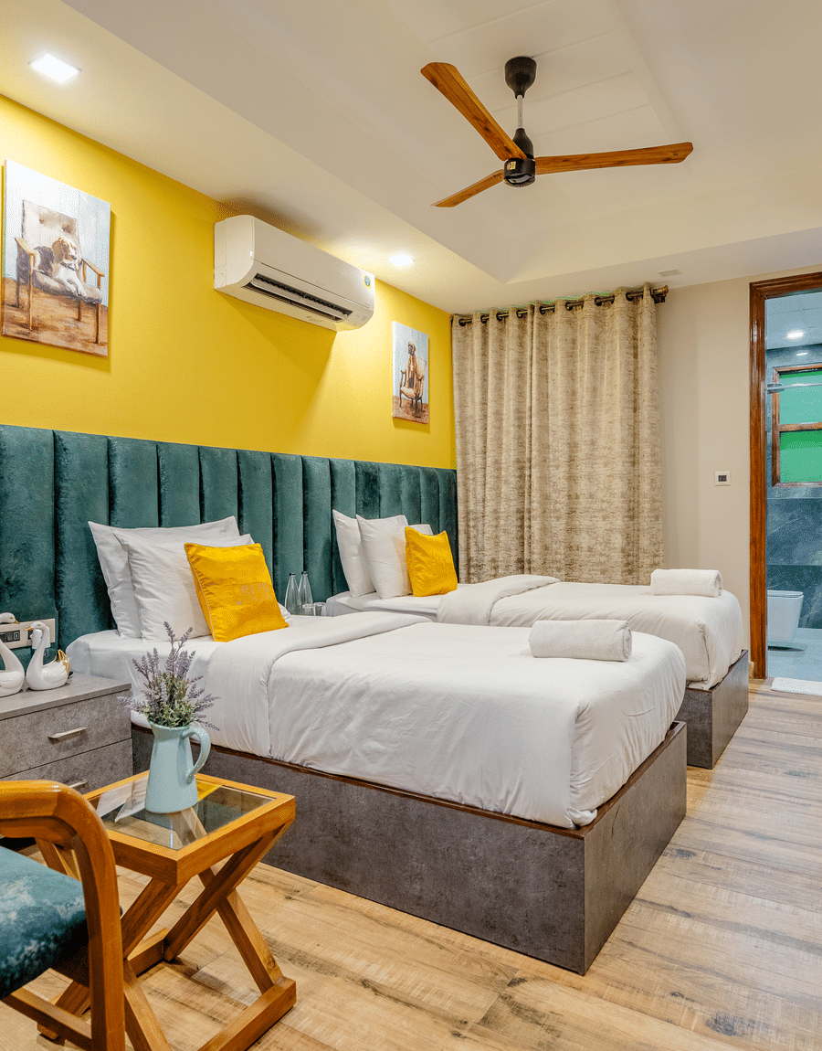 Twin beds with yellow cushions below a yellow accent wall in the Deluxe Twin Room at Lime Tree Hotel Near Medanta