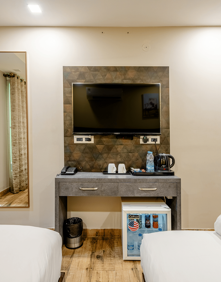 Wall-mounted TV above a console with a kettle and minibar in the Deluxe Twin Room at Lime Tree Hotel Near Medanta