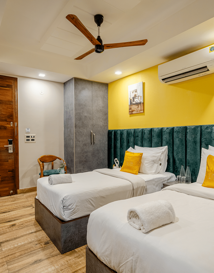 Twin beds with a teal tufted headboard beside a wooden door in the Deluxe Twin Room at Lime Tree Hotel Near Medanta