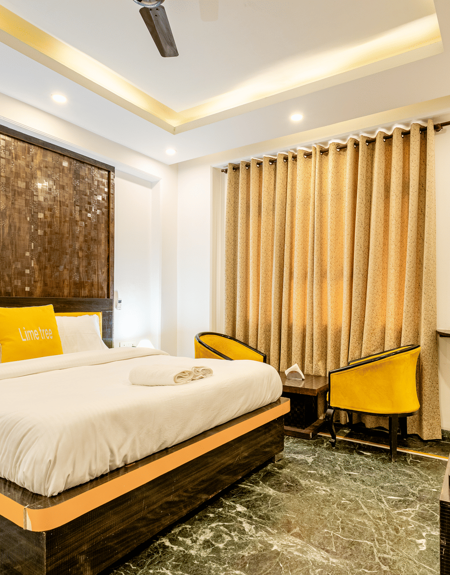 King bed, two yellow armchairs and gold curtains in the Superior King Room at Lime Tree Hotels and Banquet Hall, Huda Metro