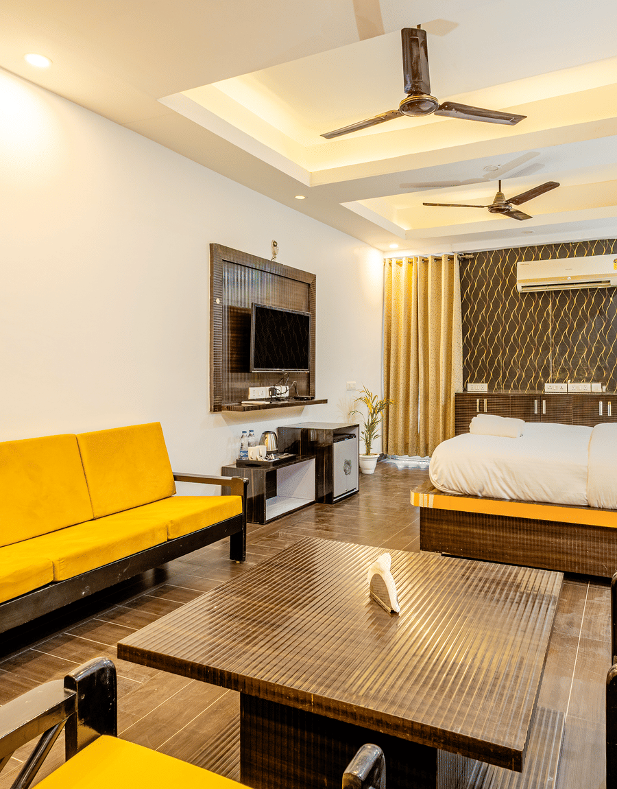 Yellow sofa and king size bed facing the TV at Lime Tree Hotels and Banquet Hall Near Huda Metro, Gurgaon