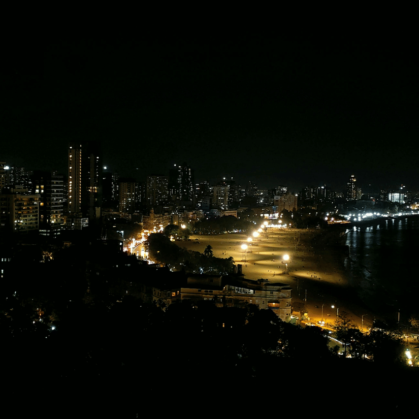 Panoramic night view of Mumbai's Marine Drive coastline with illuminated city skyline and curved shoreline