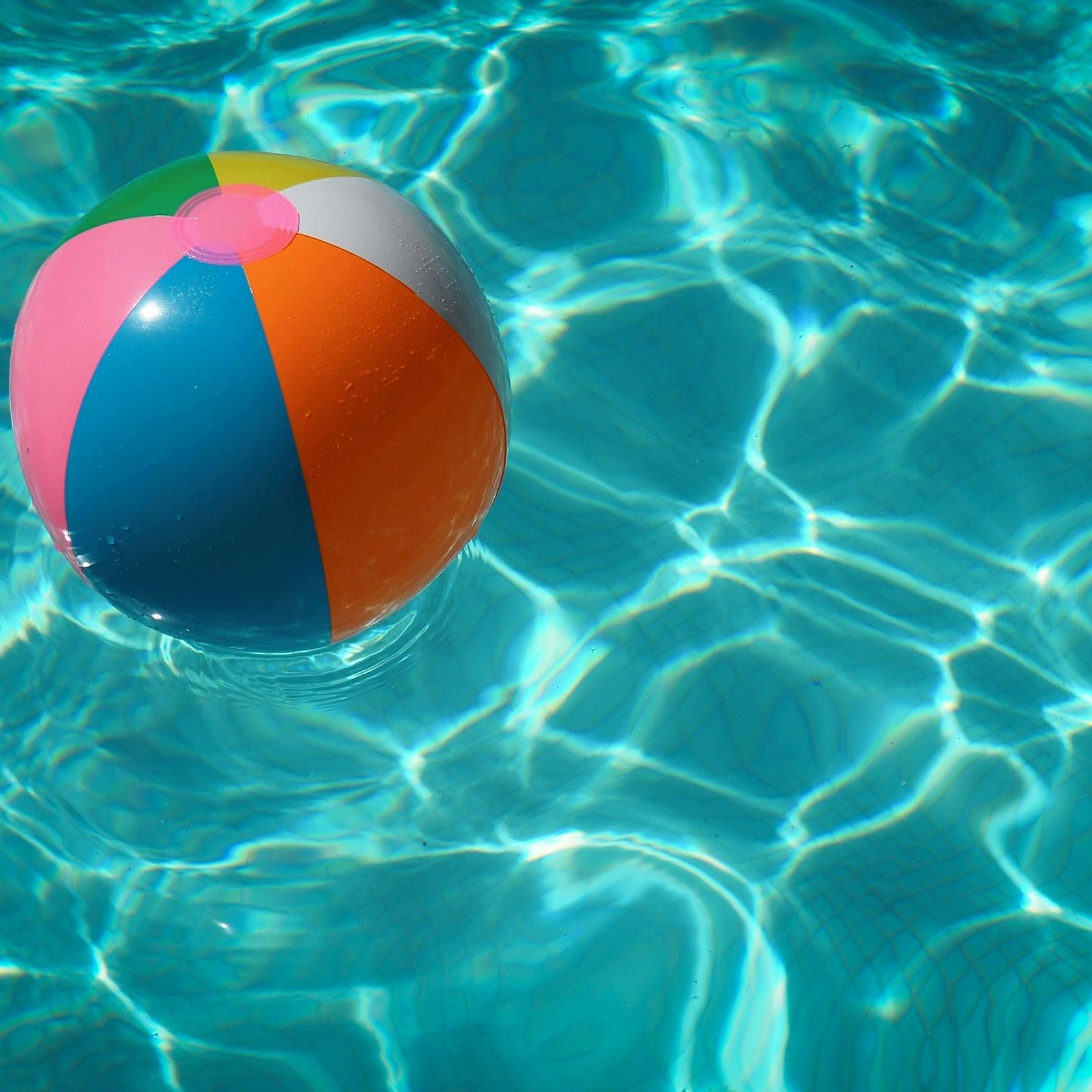 A colorful beach ball floating in a clear blue swimming pool, reflecting the sunlight and creating a vibrant, playful scene.