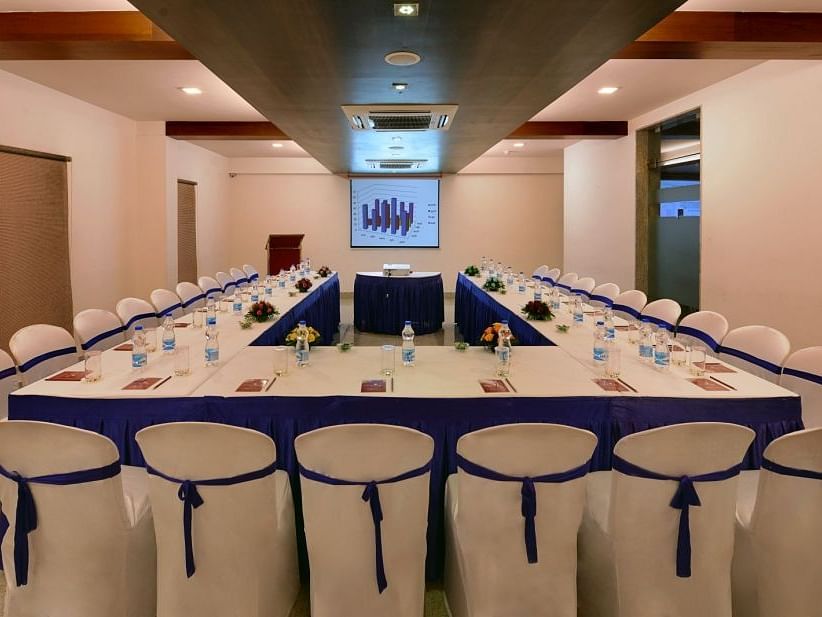 A long conference table with chairs, water bottles, and presentation materials in a meeting room with a projector screen.
