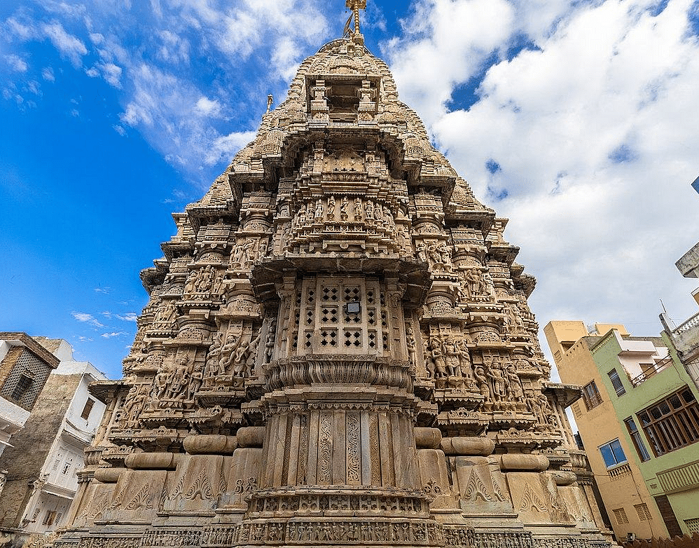 A tall, intricately carved stone temple against a sky with white clouds. 