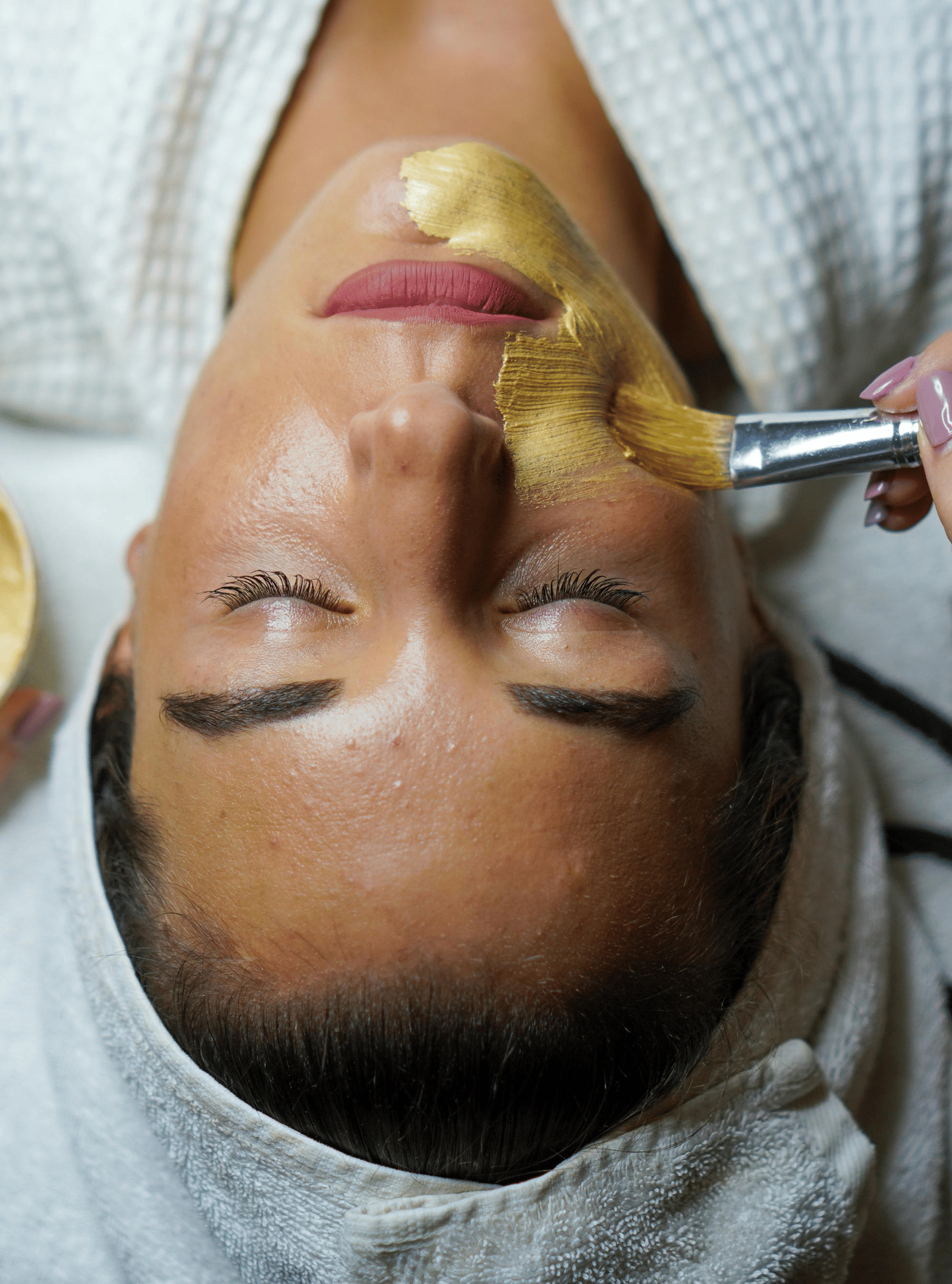 Woman receiving a facial treatment with a golden face mask applied.