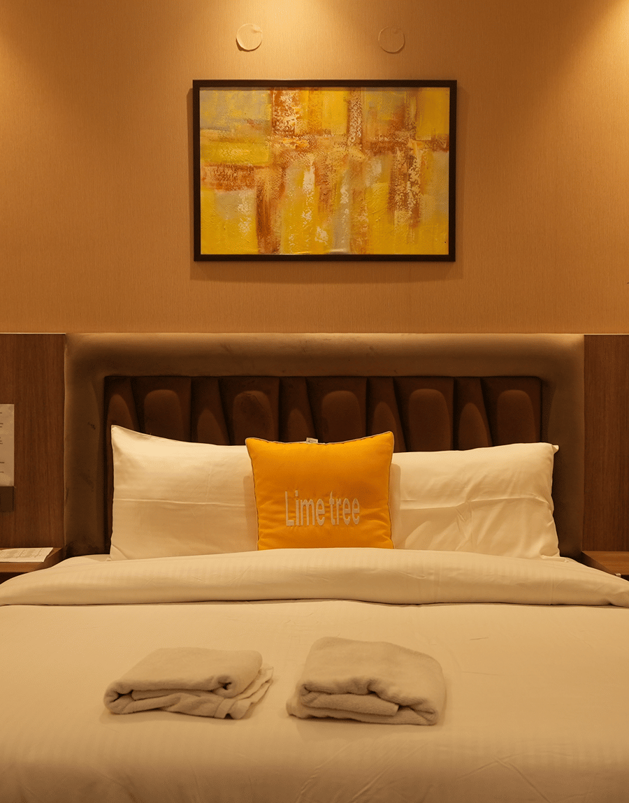 King bed with a yellow cushion below an abstract painting in the Executive Suite at Lime Tree Hotel Near India Expo Mart