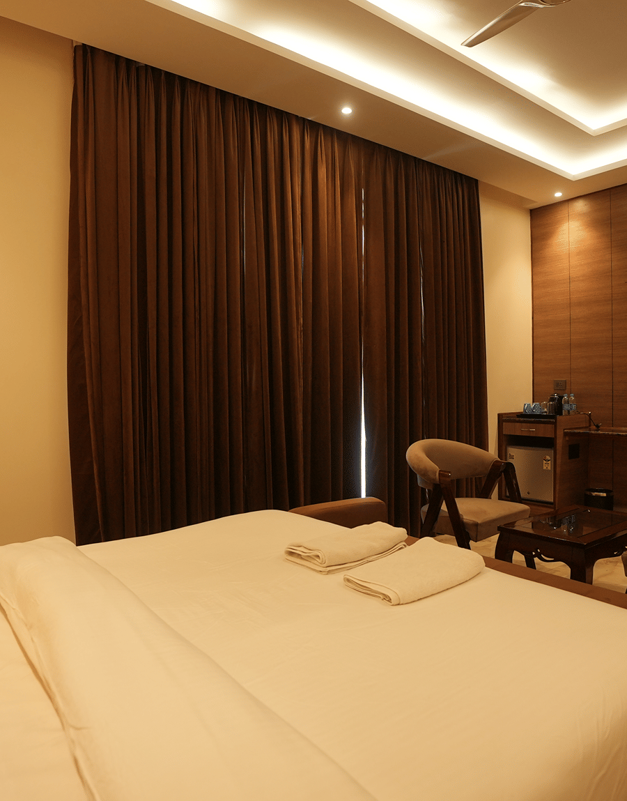 King bed, brown curtains and a seating corner in the Executive Suite at Lime Tree Hotel Near India Expo Mart