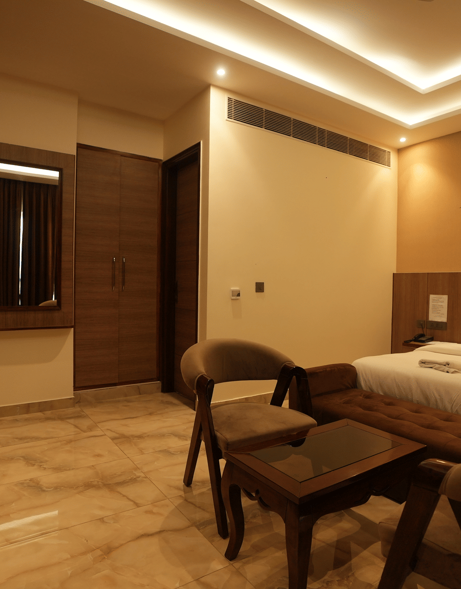 Seating corner with wooden chairs and a glass table in the Executive Suite at Lime Tree Hotel Near India Expo Mart