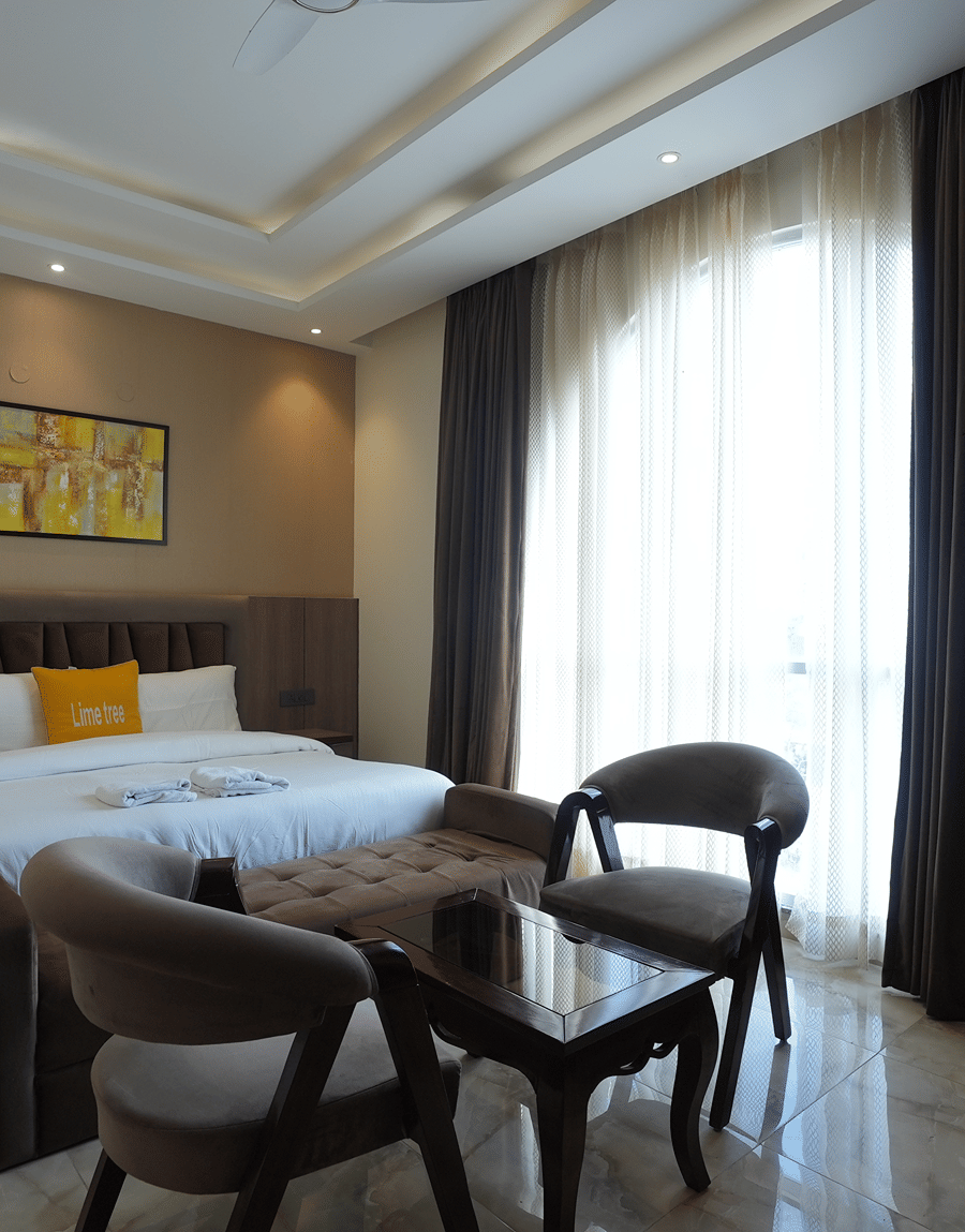 King bed with a yellow cushion, armchairs and sheer curtains in the Executive Suite at Lime Tree Hotel Near India Expo Mart