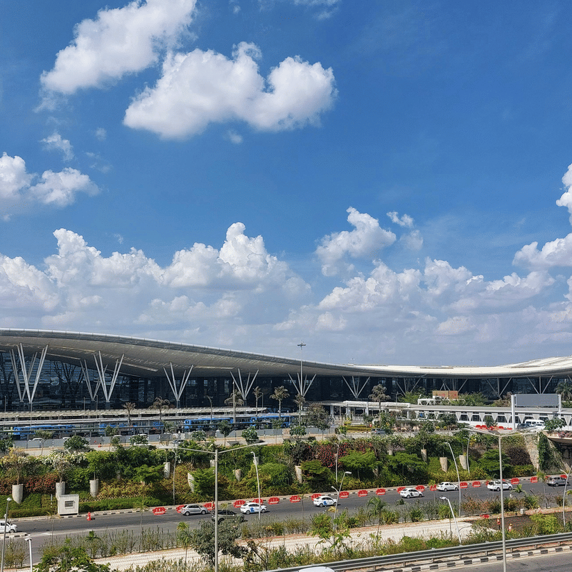 A far-out view of the Terminal 1 of Kempegowda International Airport, where Bangalore to Kolkata flights take off, with a bridge, roads, cars, lawn area and a pole with the Indian flag on it