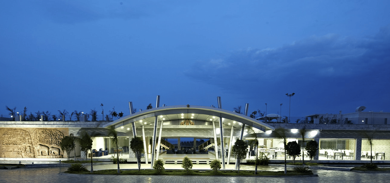 The entrance of Grande Bay Resort & Spa, Mamallapuram, illuminated with bright lights, with the dining area on the right and a view of Arjuna’s Penance on the left.