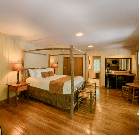 a cozy bedroom with a wall mounted art piece besides a double bed and a dressing table at the far end of the room - Historic Tapoco Lodge