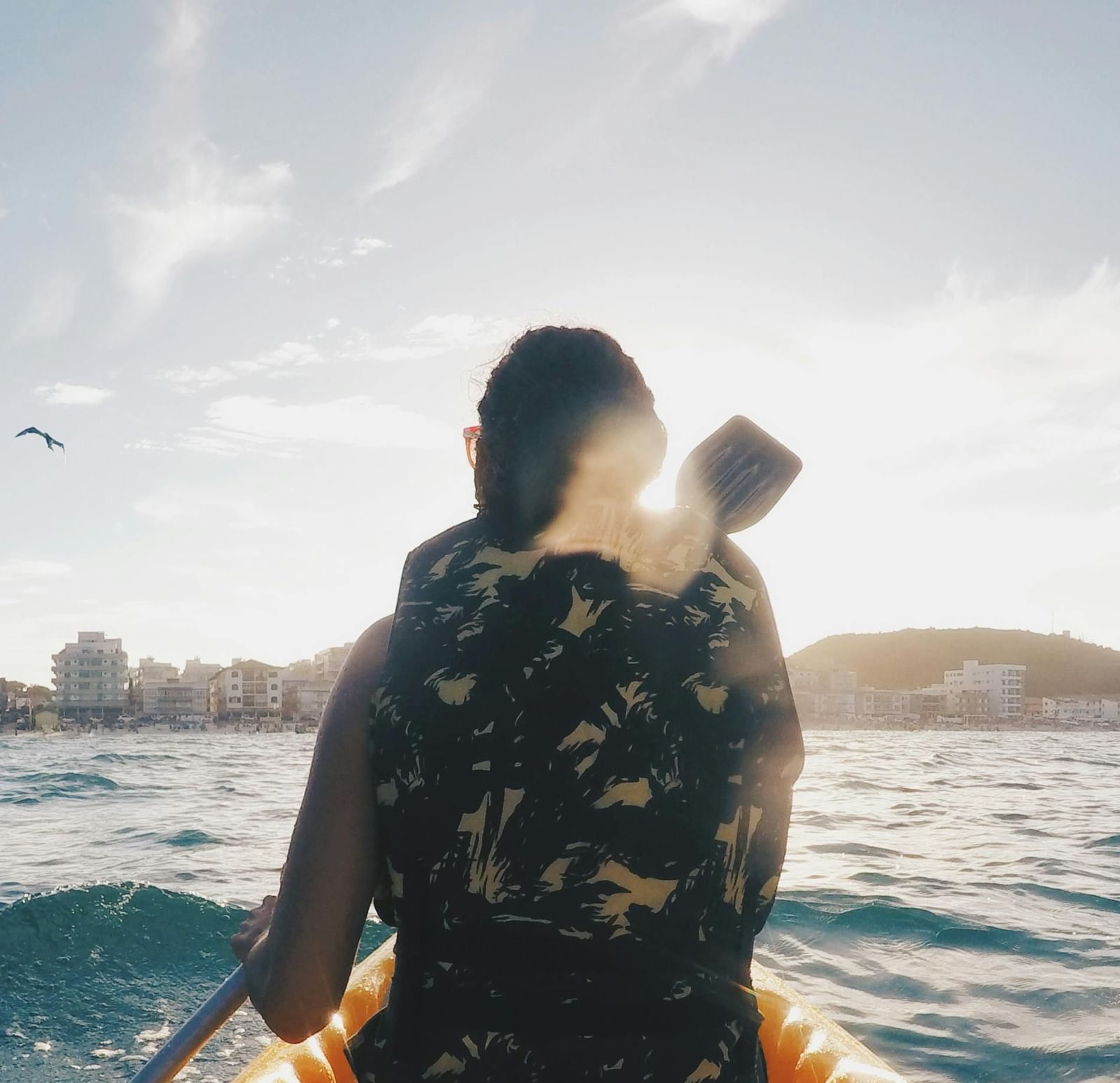A traveller kayaking through calm blue waters, facing the horizon under a bright, clear sky.