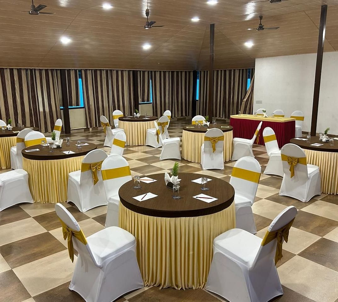 An indoor banquet hall is prepared for an event, with round tables and chairs neatly arranged | Ballroom | Woodstock Resorts, Coorg