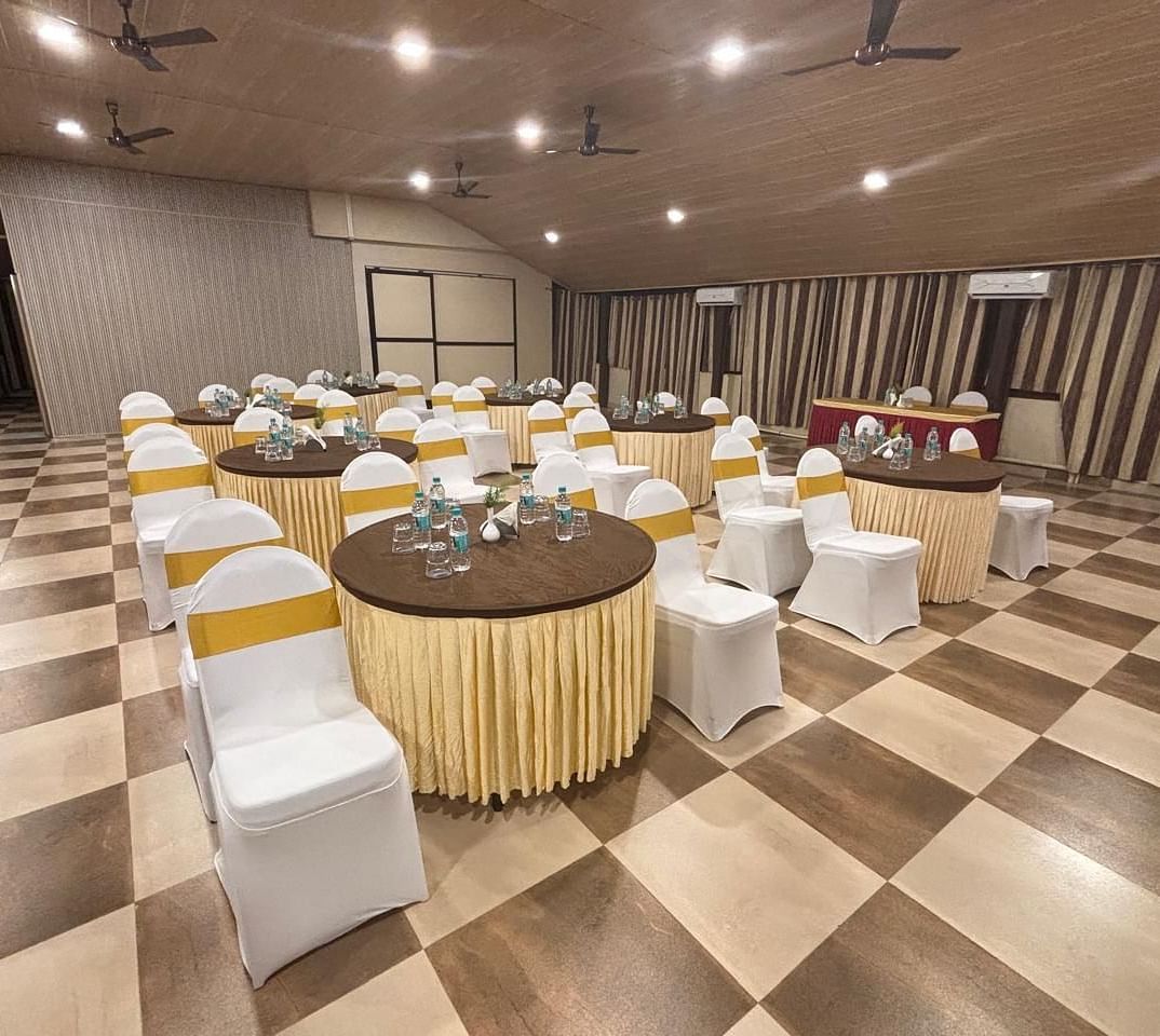 A banquet hall setup with round tables and chairs neatly arranged under ambient lighting | Ballroom | Woodstock Resorts, Coorg | Woodstock Resorts, Coorg